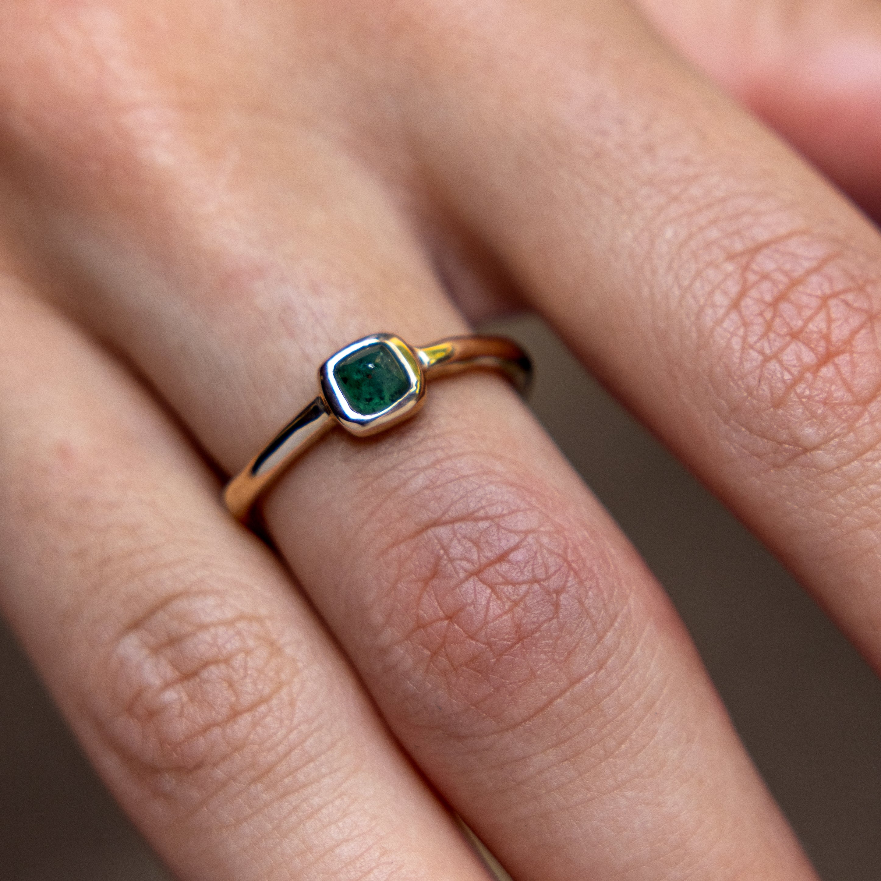 Close up of a hand wearing the Cosmos Emerald Ring in solid recycled gold.