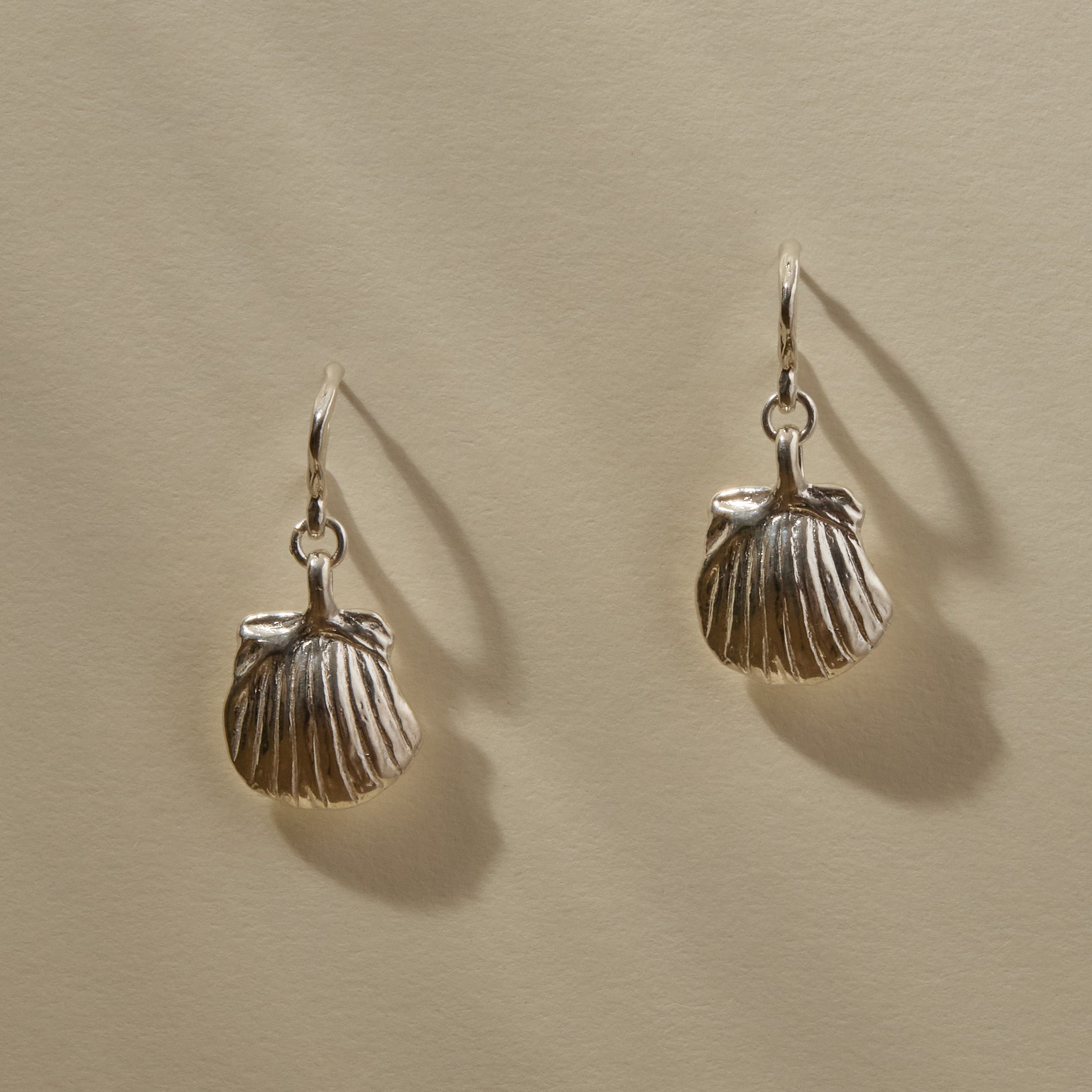 Elysian Shell Hoop Earrings in sterling silver hanging side by side, scallop shells below small hoops.