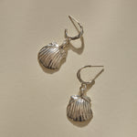 Elysian Shell Hoop Earrings in recycled sterling silver, cast scallop shells on slim hoops, laid flat.