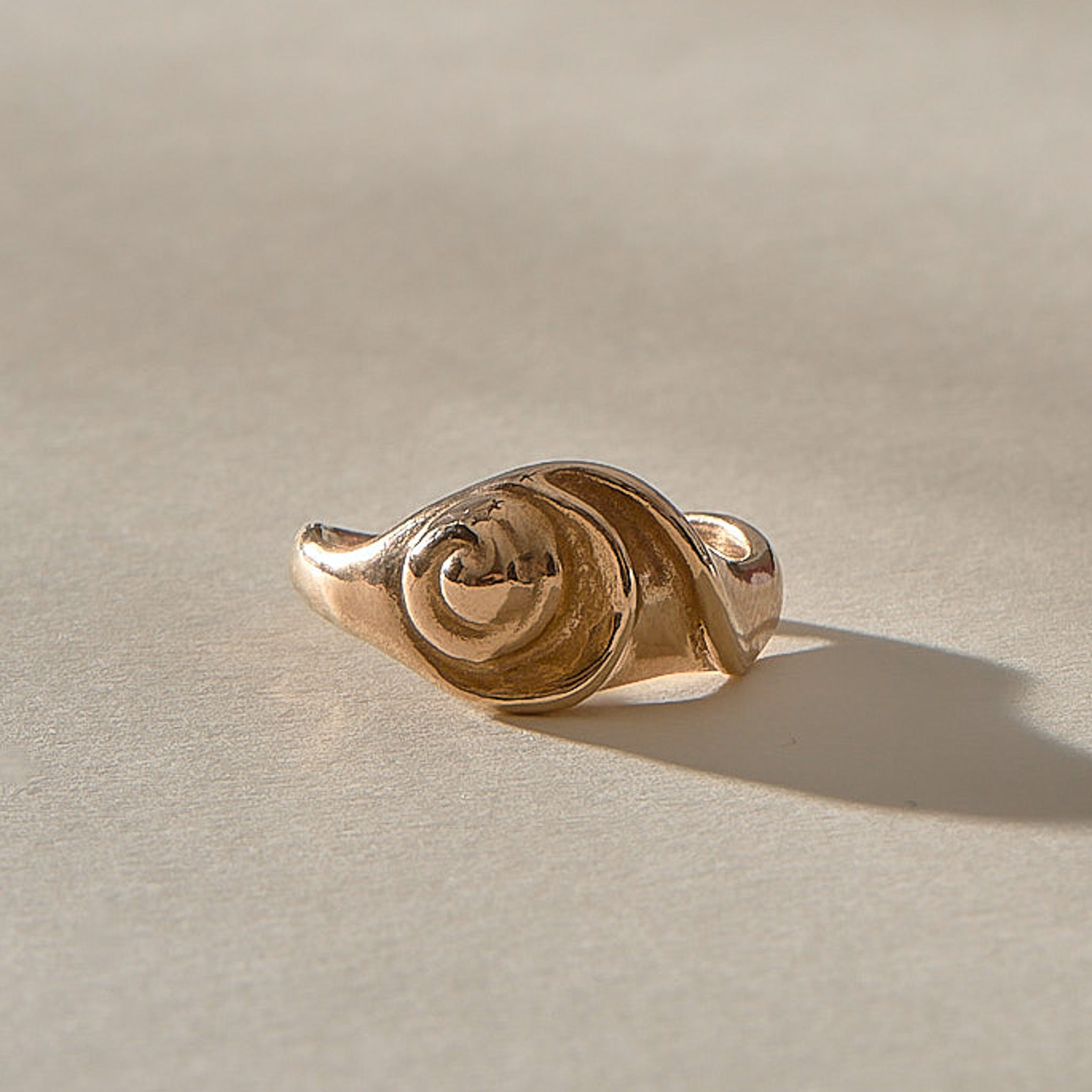 Neptune Spiral Shell Ring in bronze from a low angle, the spiral shell rising from the band.