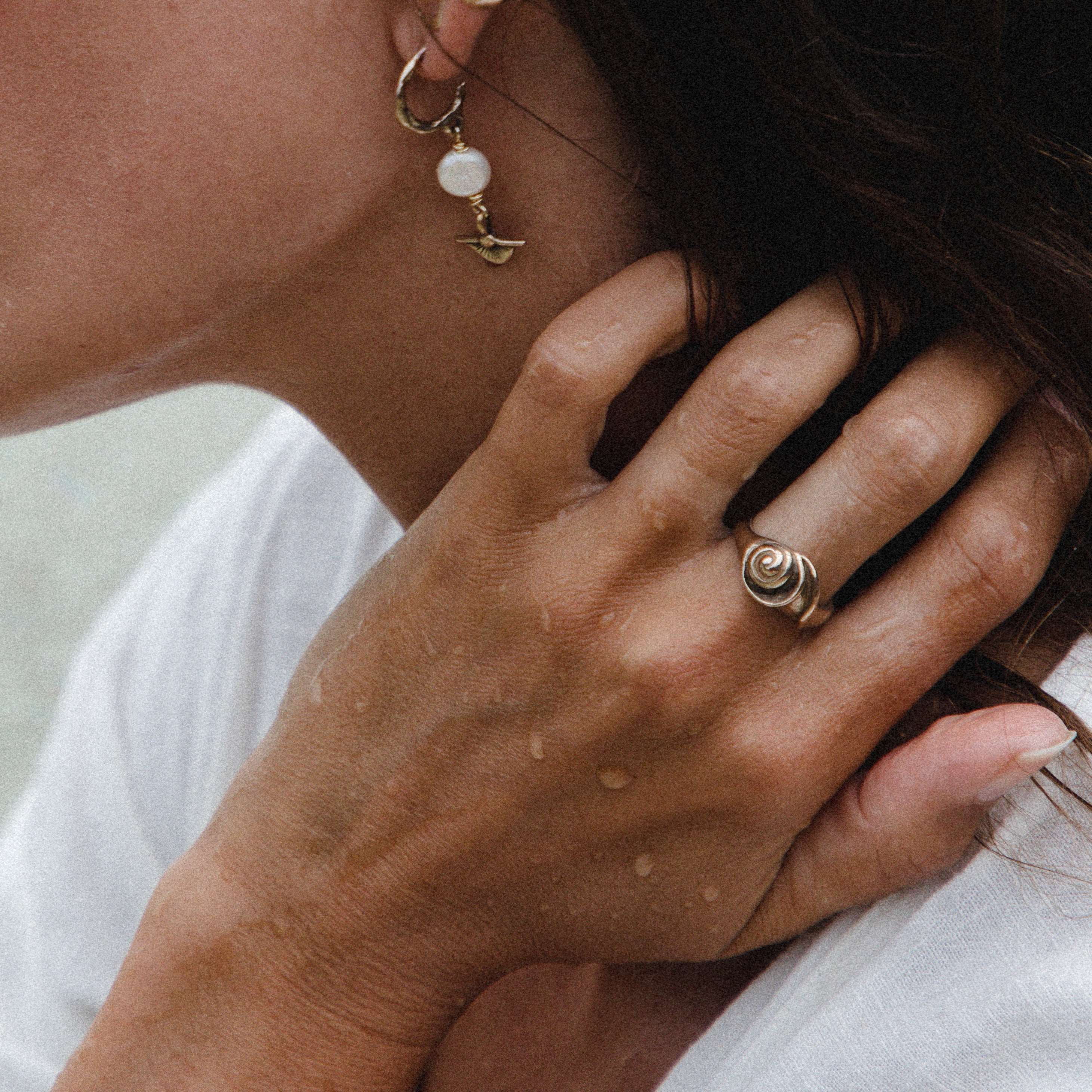 Neptune Spiral Shell Ring worn on the hand, fingers in the model's hair.