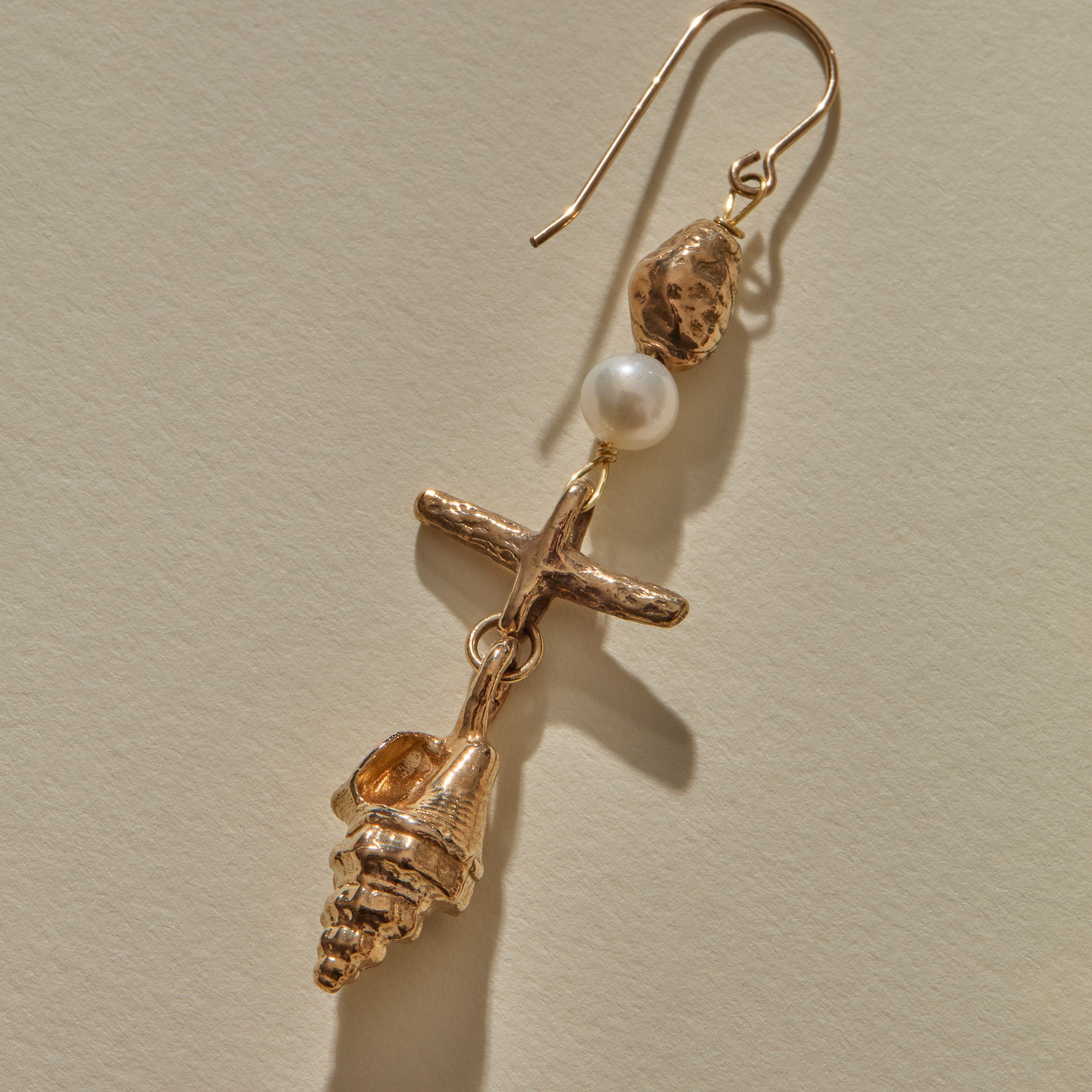 Close view of a Sereia Shell and Pearl Chandelier Earring in bronze, the pearl above the ridged spiral shell.
