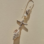 Close view of a Sereia Shell and Pearl Chandelier Earring in sterling silver, the pearl above the ridged spiral shell.