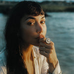 Model by the water with her hand at her lips, wearing the Heart of the Sun Statement Ring.