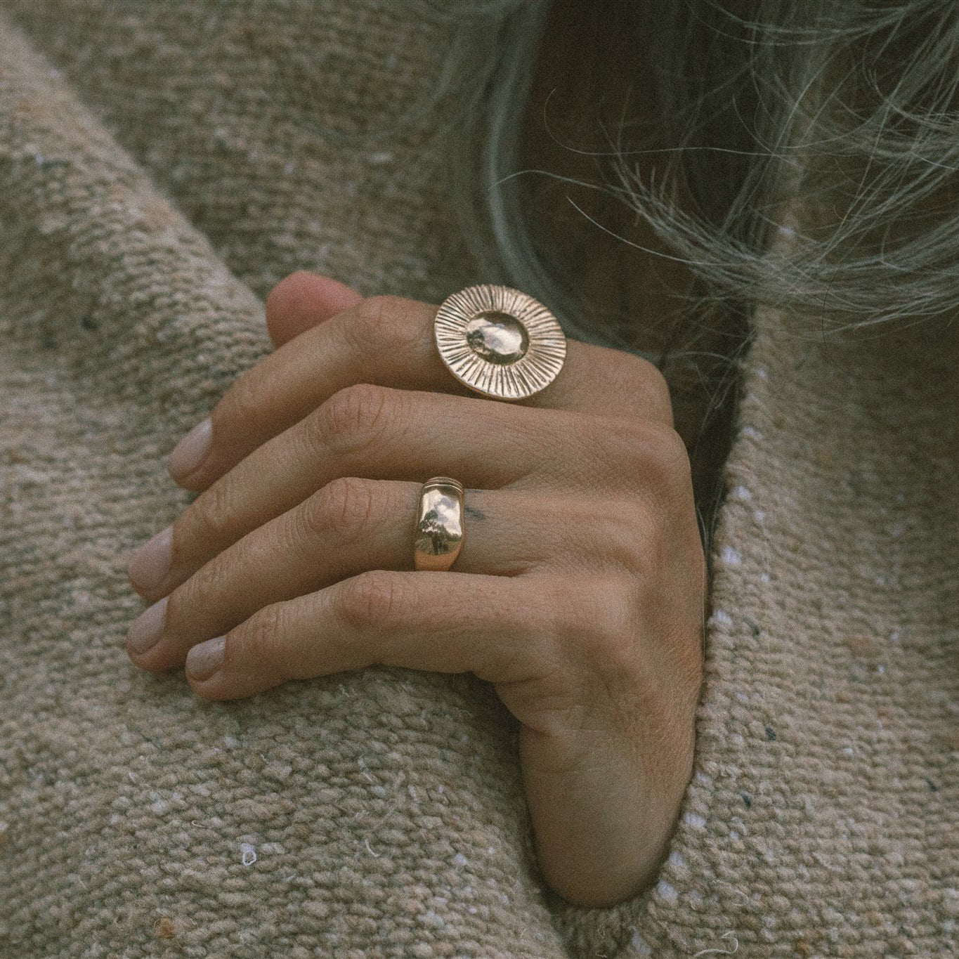 Hand resting on a knit sweater, wearing the Heart of the Sun Statement Ring stacked with a slim ring.