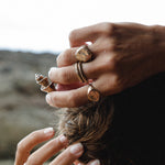 Hands gathering long hair, wearing the Heritage Textured Signet Ring stacked with other rings.